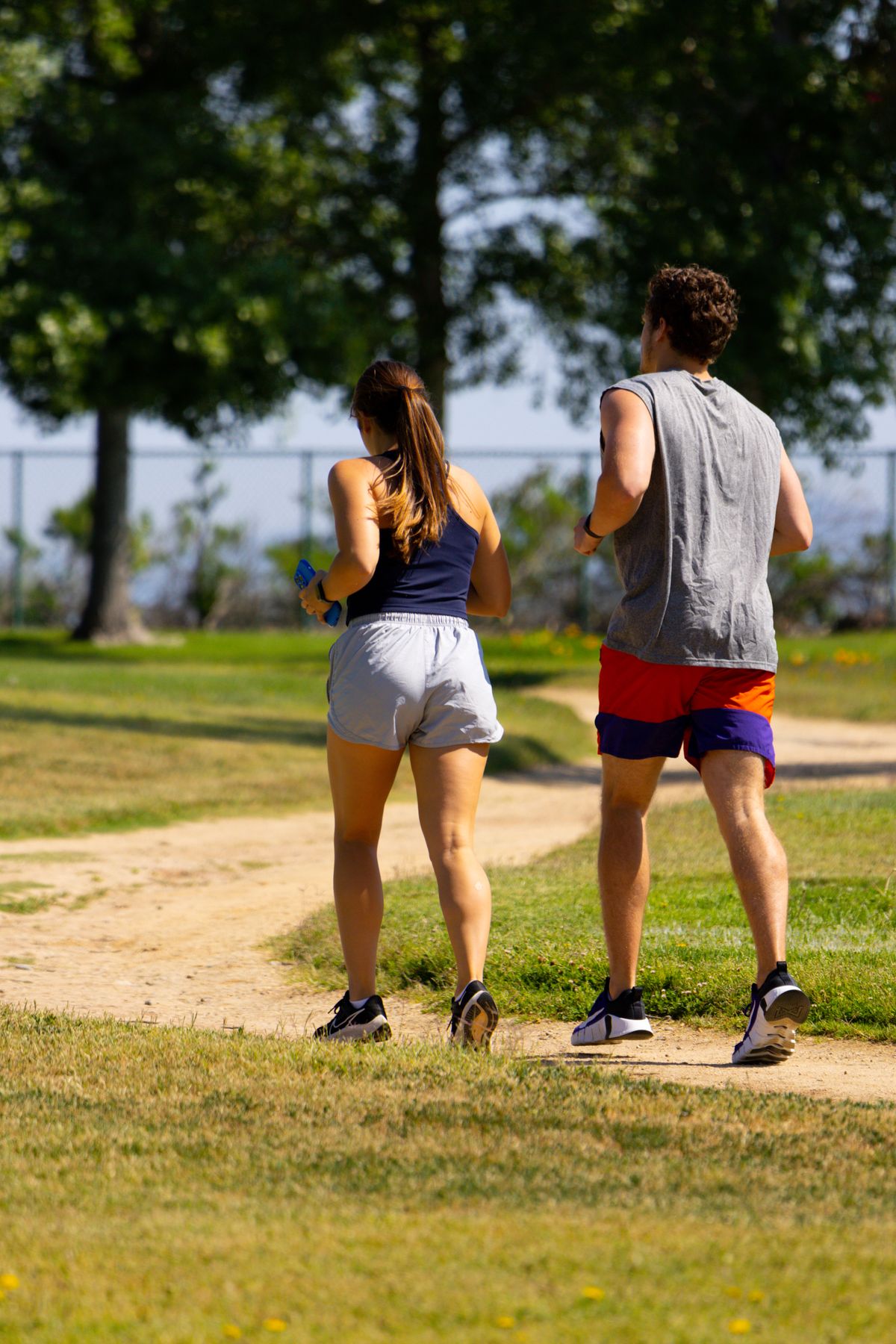 Deux personnes courent côte à côte sur un chemin de parc ensoleillé.