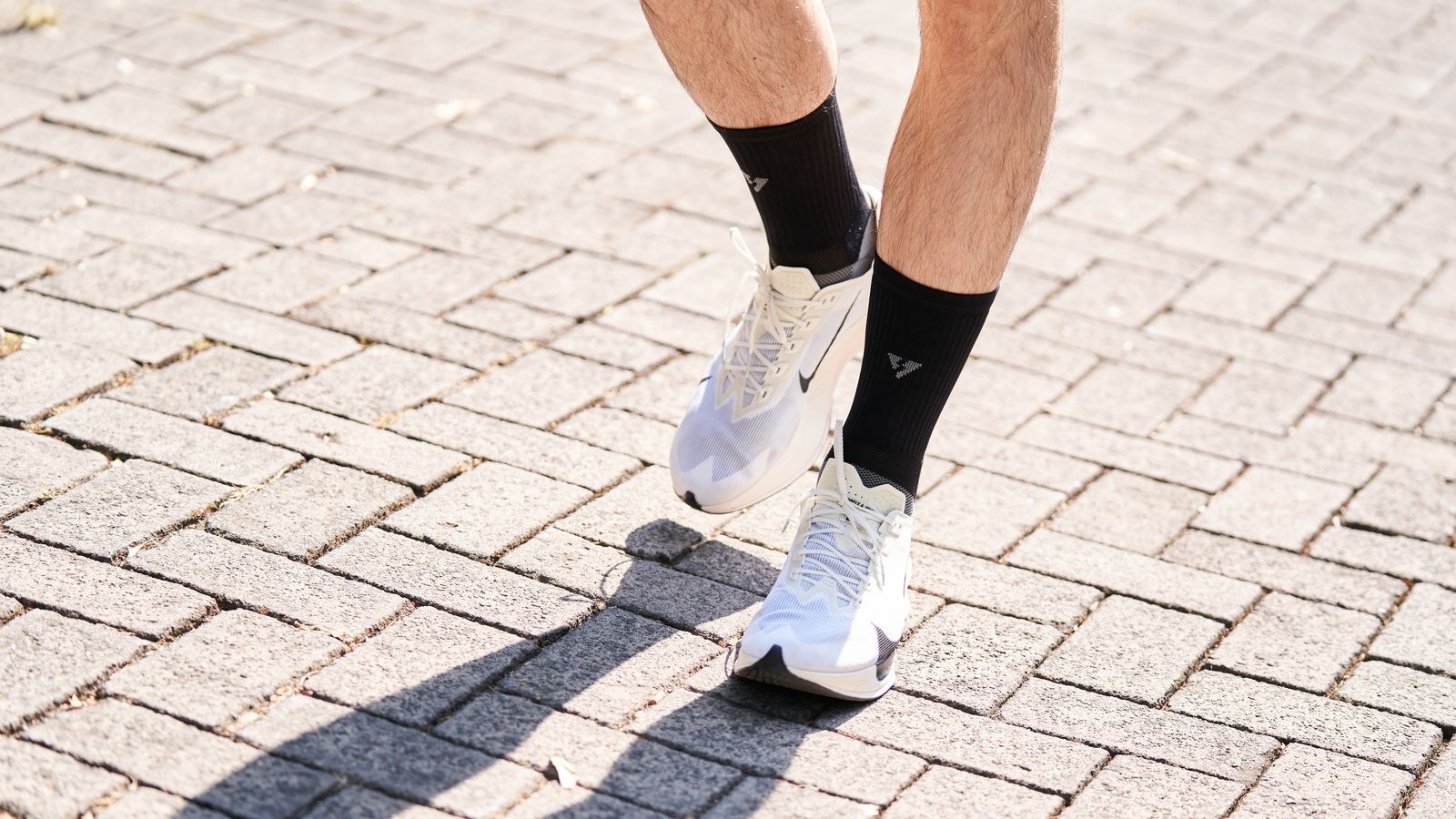 Une personne en chaussures de course marche sur une allée pavée.