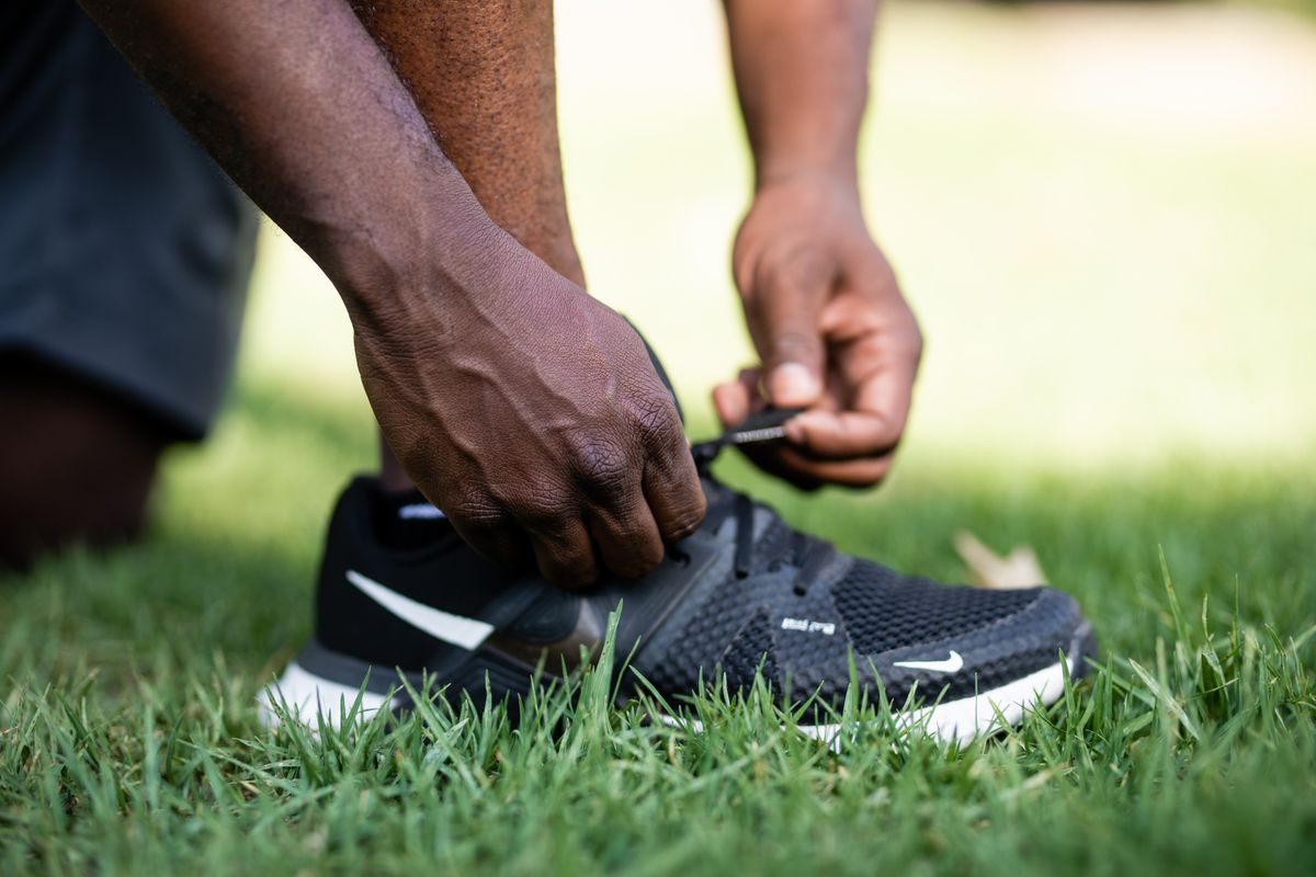 Des mains ajustent les lacets d’une chaussure de course noire sur l’herbe.